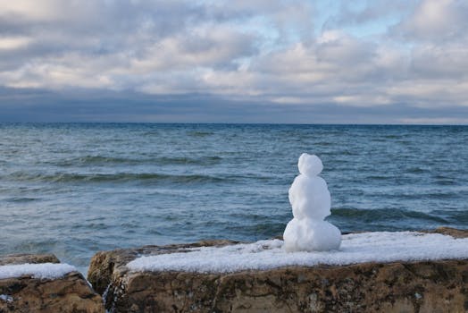 Snowman on rocky shore with a vibrant winter sky in Southampton, Ontario, Canada.