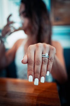 Close-up shot of a woman's hand displaying her engagement and wedding rings with manicured nails.