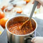 A person stirring a pot of homemade chili stew on a stovetop, capturing the essence of home cooking.
